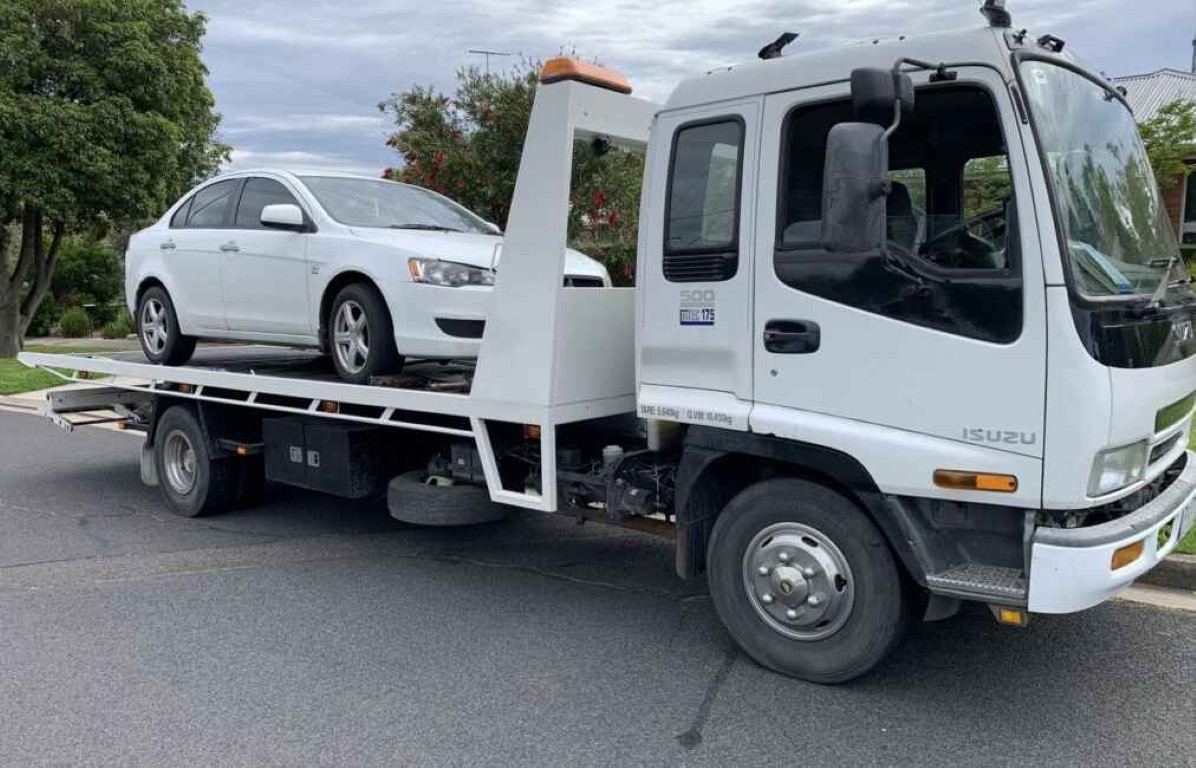 White flatbed tow truck transporting sedan for long-distance towing in Gilroy, CA